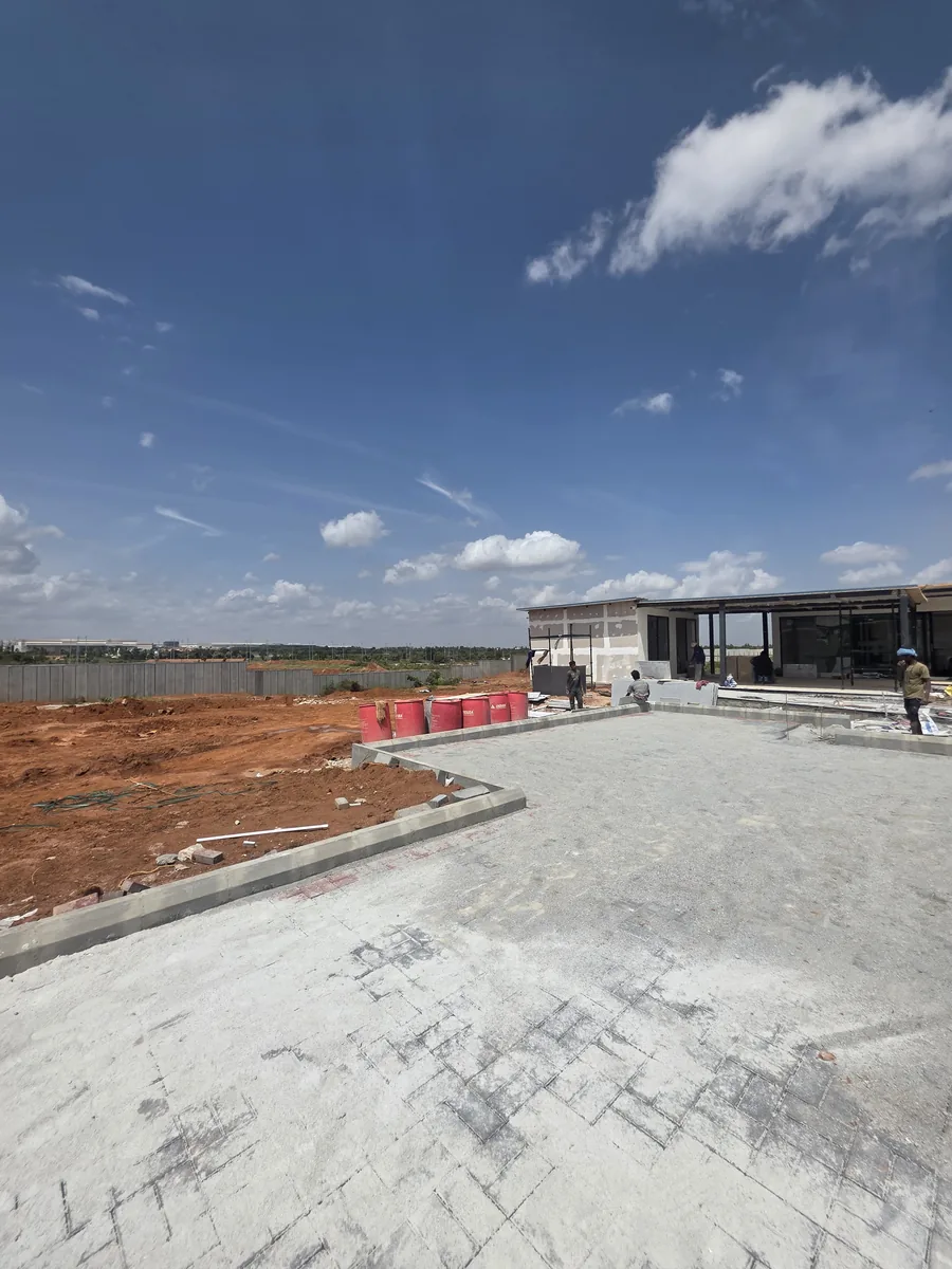Prestige Park Lane experience centre under construction with cast forecourt slab and glazed pavilion, Devanahalli, August 2026