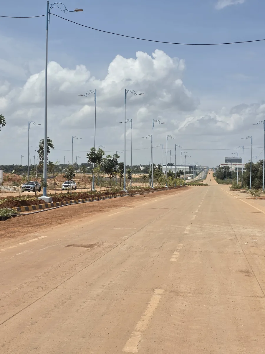 Concrete approach road with new street lighting and planted median at KIADB Aerospace Park Phase 2, Devanahalli, serving Prestige Park Lane, August 2026